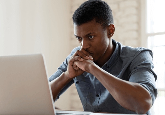 Safety and Security A man sitting worriedly at his desktop looking at his laptop